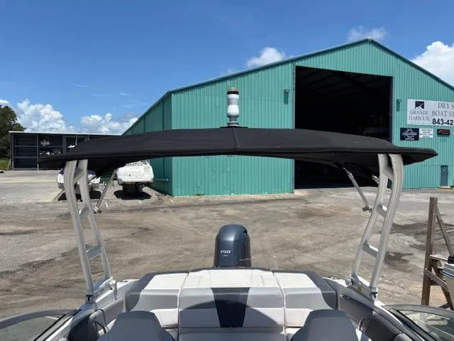 Slide: The Image of 2019 Chaparral 210 Deluxe boat with canopy, parked near a green warehouse. - 15