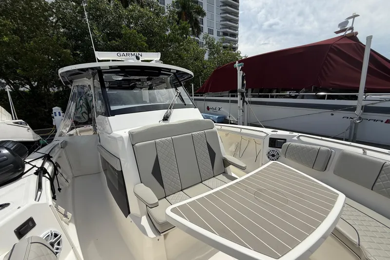 Slide: The Image of 2022 Pursuit S 358 Sport boat with luxurious seating and table, docked near modern buildings. - 43