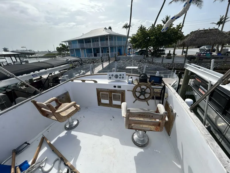 Slide: The Image of 1978 Albin 36 Trawler helm with wooden chairs and steering wheel, docked near a coastal building. - 39