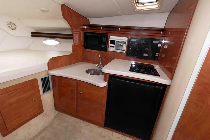 Slide: The Image of 2004 Rinker Fiesta Vee 342 boat interior with kitchenette, featuring wood cabinetry and modern appliances. - 12