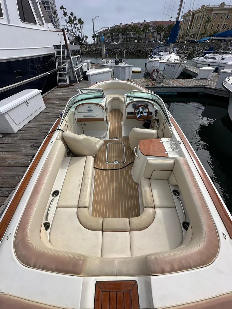 Slide: The Image of 2008 Chris-Craft Launch 25 boat interior with beige seating and wooden accents at a marina. - 8