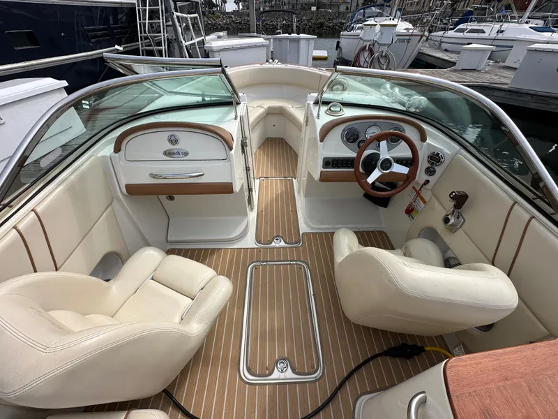 Slide: The Image of 2008 Chris-Craft Launch 25 boat interior with beige seating and wooden accents at a marina. - 9