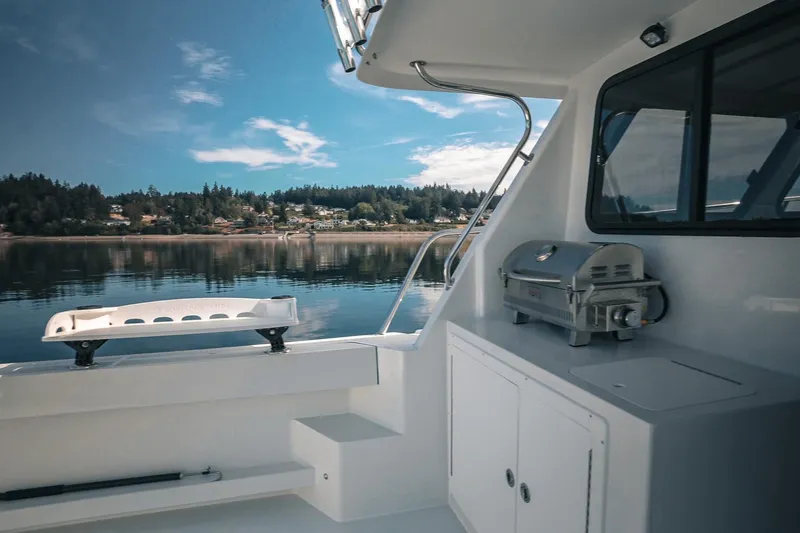 Slide: The Image of Lindell 41' 2027 boat deck with grill, overlooking serene waters and forested shoreline. - 16