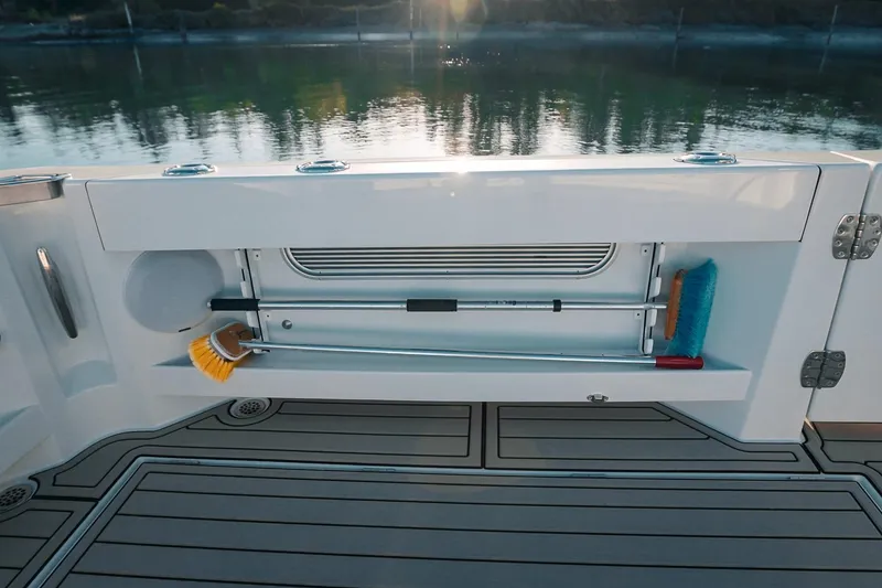 Slide: The Image of Storage compartment on a 2027 Lindell 42' boat, featuring cleaning tools and a serene water backdrop. - 13