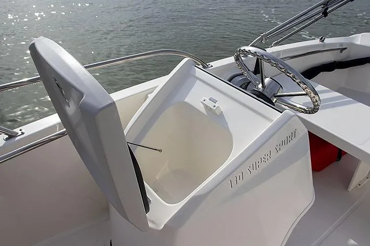 Slide: The Image of 2025 Boston Whaler 130 Super Sport boat interior with open storage compartment and steering wheel. - 6