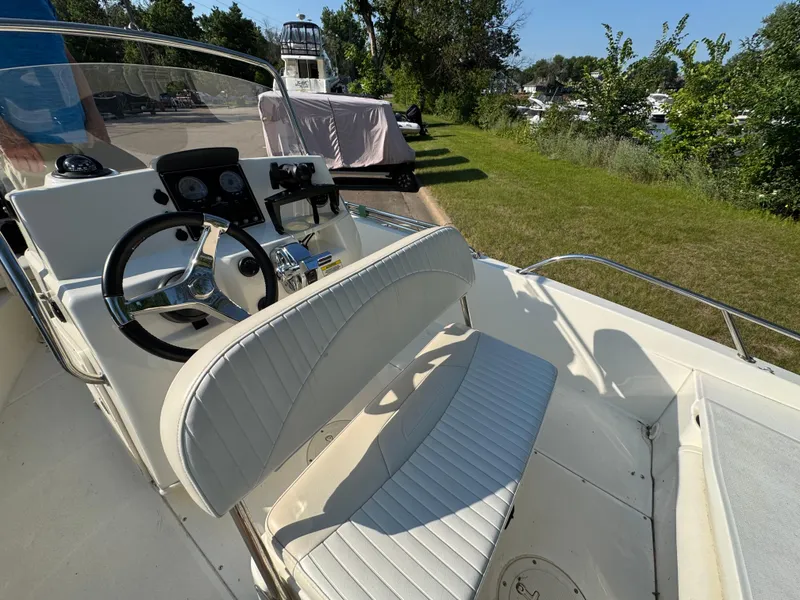 Slide: The Image of 2011 Boston Whaler 180 Dauntless boat interior with steering wheel and seating, docked near greenery. - 19