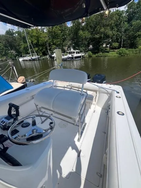 Slide: The Image of 2004 Boston Whaler 270 Outrage boat interior with steering wheel, white seating, and river backdrop. - 16