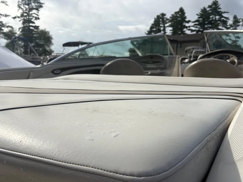 Slide: The Image of 2003 Sea Ray 200 Bow Rider interior with beige upholstery and open windshield, docked near trees. - 6