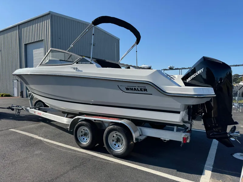 Slide: The Image of 2025 Boston Whaler 210 Vantage boat on trailer, parked outdoors. - 2