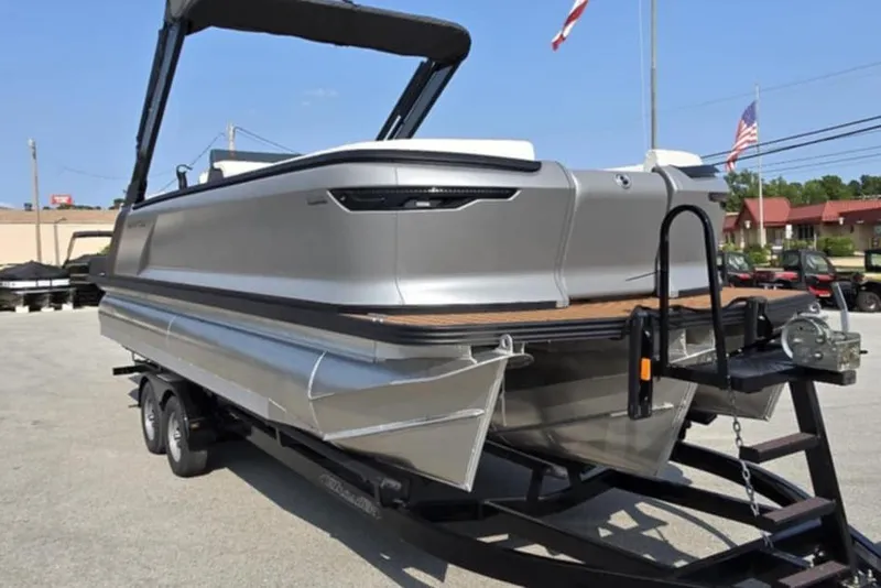 Slide: The Image of 2025 Manitou Explore pontoon boat on trailer, sleek design, outdoor setting. - 2