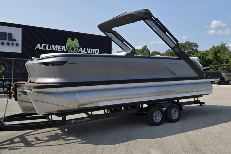 Slide: The Image of 2025 Manitou Explore pontoon boat on trailer at Acumen Audio dealership. - 3