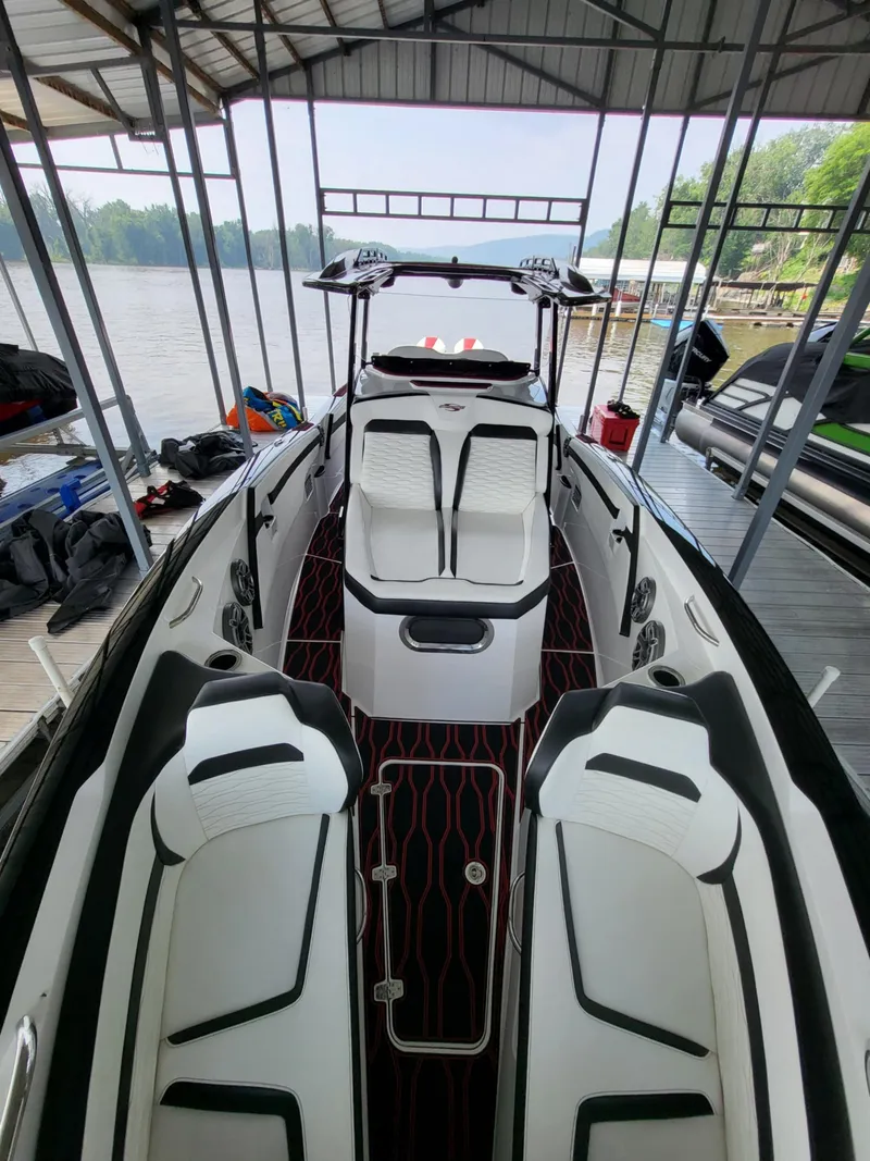 Slide: The Image of 2023 Sunsation 32 CCX boat interior with white seating and red-accented flooring, docked by a lake. - 17