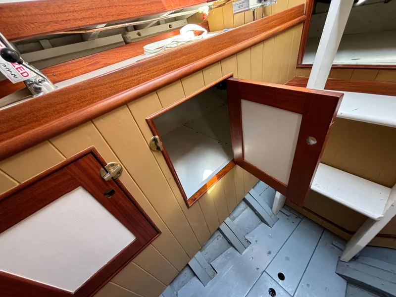 Slide: The Image of Interior of a 1951 Custom Pilot Cutter with open wooden cabinets and stairs. - 13