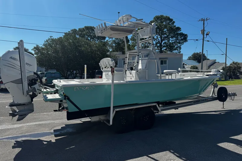 Slide: The Image of 2019 Dorado 25 Flat Deck boat with outboard motor, parked near a marina under clear blue skies. - 3