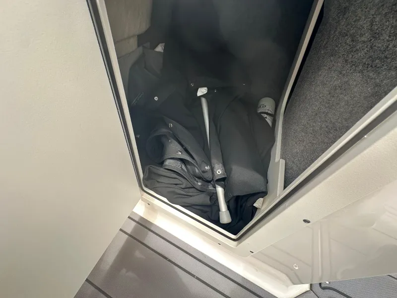 Slide: The Image of Storage compartment in 2023 Chaparral 21 SSi OB boat, containing black clothing and a metal rod. - 15