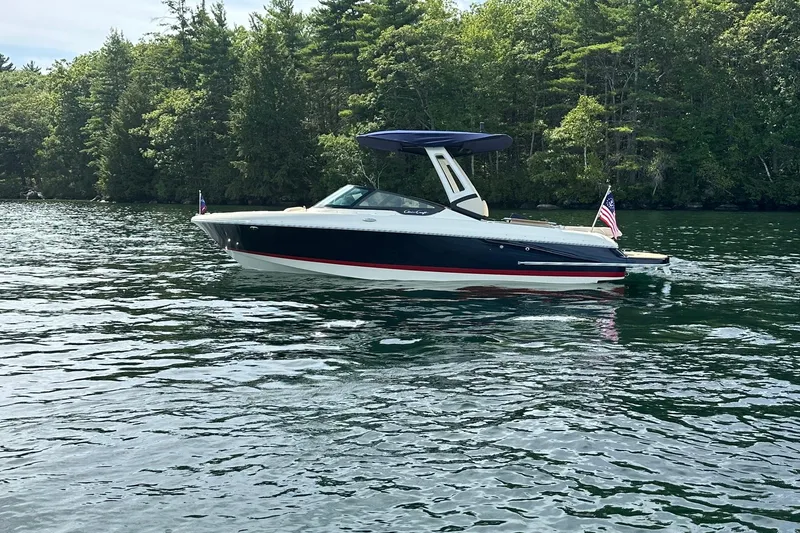 Slide: The Image of 2026 Chris-Craft Sportster 25 boat on a serene lake with lush green trees. - 2