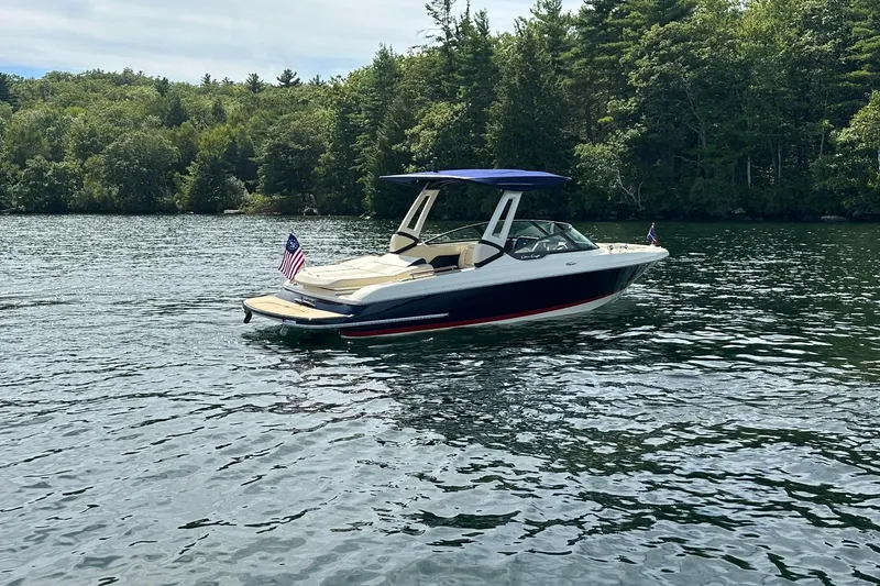Slide: The Image of 2026 Chris-Craft Sportster 25 boat on a serene lake with lush green forest backdrop. - 4
