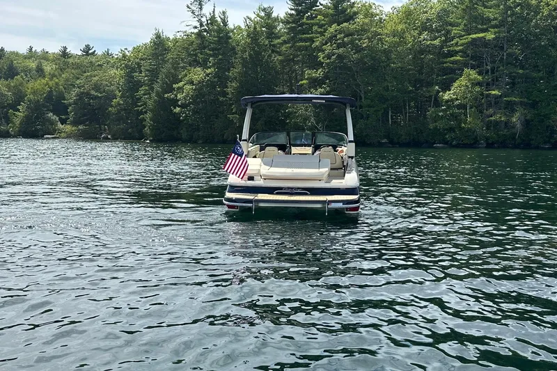 Slide: The Image of 2026 Chris-Craft Sportster 25 boat on a lake, American flag, surrounded by trees. - 6