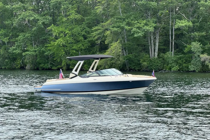 Slide: The Image of 2026 Chris-Craft Sportster 25 boat on a serene lake, surrounded by lush greenery. - 12