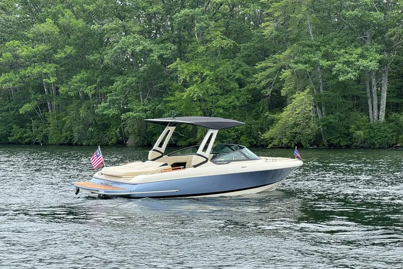 Slide: The Image of 2026 Chris-Craft Sportster 25 boat on a serene lake with lush green forest backdrop. - 10