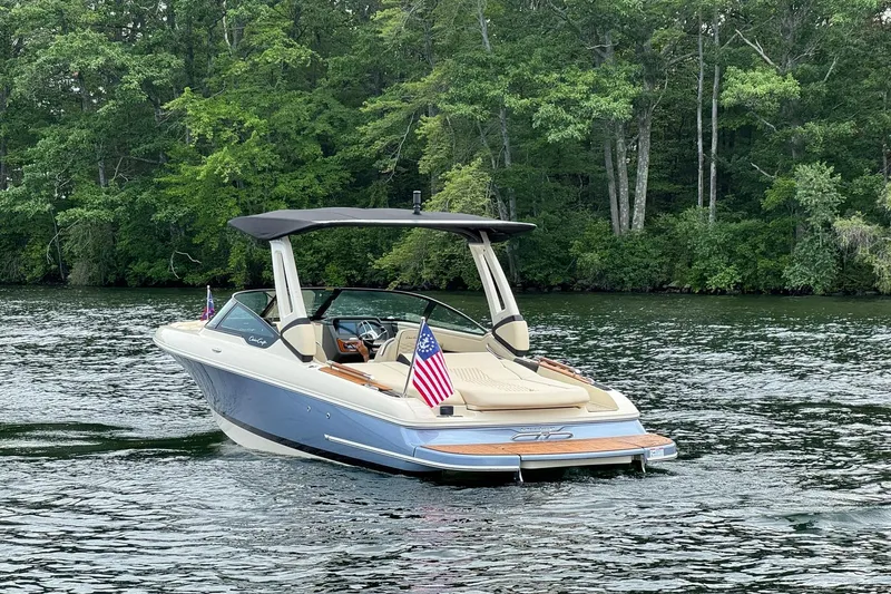 Slide: The Image of 2026 Chris-Craft Sportster 25 boat on a serene lake with lush green forest backdrop. - 6
