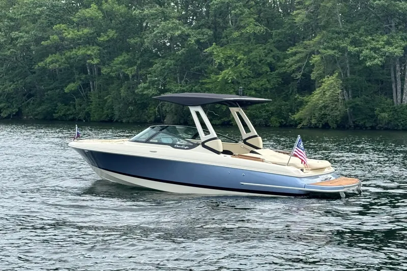 Slide: The Image of 2026 Chris-Craft Sportster 25 boat cruising on a serene lake with lush green trees. - 5