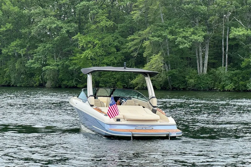 Slide: The Image of 2026 Chris-Craft Sportster 25 boat on a serene lake with lush green forest backdrop. - 7