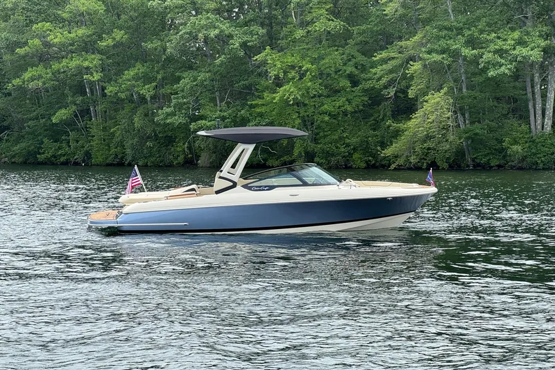 Slide: The Image of 2026 Chris-Craft Sportster 25 boat on a serene lake with lush green forest backdrop. - 11
