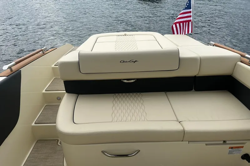 Slide: The Image of 2026 Chris-Craft Sportster 25 boat with beige seating and American flag on water. - 32