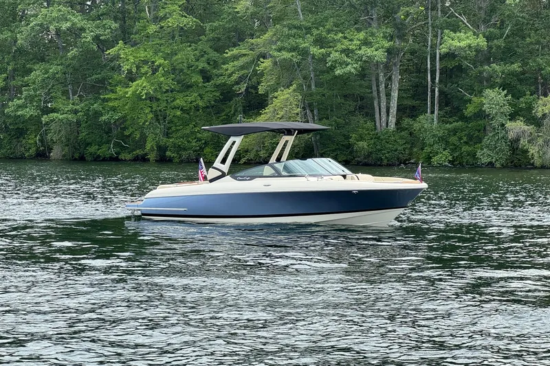 Slide: The Image of 2026 Chris-Craft Sportster 25 boat on a serene lake with lush green forest backdrop. - 13