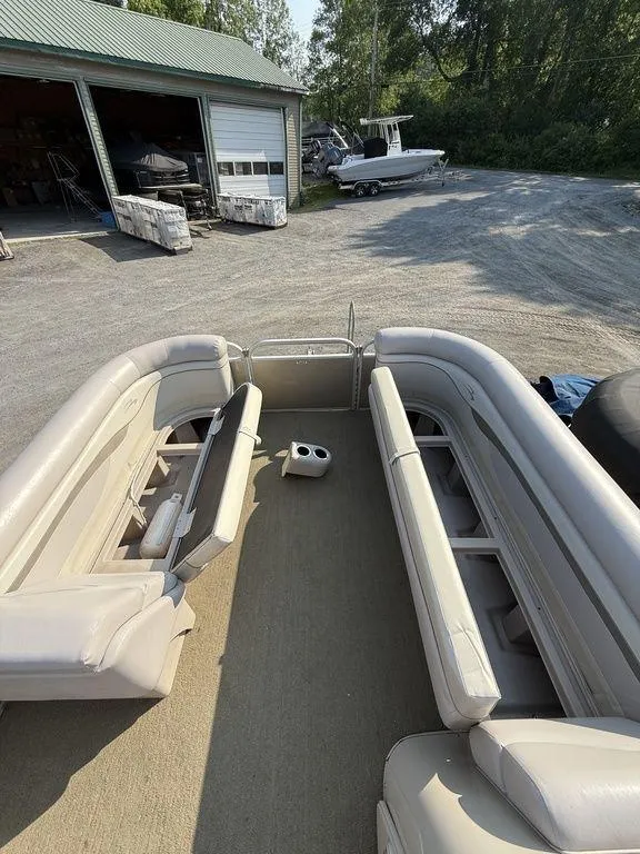 Slide: The Image of 2015 Bennington 21 SLX pontoon boat interior with beige seating, parked near a garage. - 14