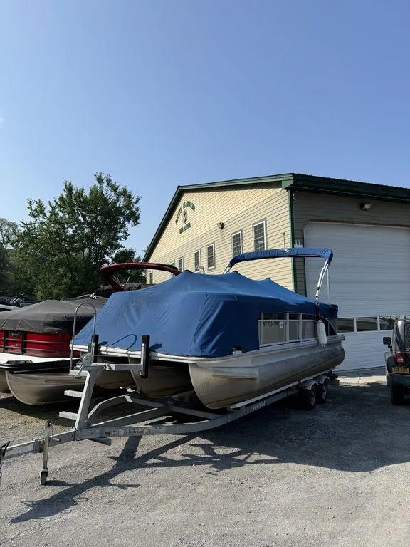 Slide: The Image of 2015 Bennington 21 SLX pontoon boat with blue cover on trailer, parked outside a building. - 6