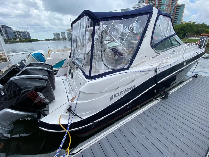 Slide: The Image of 2006 Four Winns 348 Vista boat docked with Mercury engines, clear canopy, and cityscape background. - 25