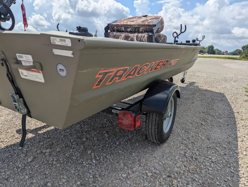 Slide: The Image of 2025 Tracker Grizzly 15 Jon boat on trailer, parked on gravel under cloudy sky. - 23