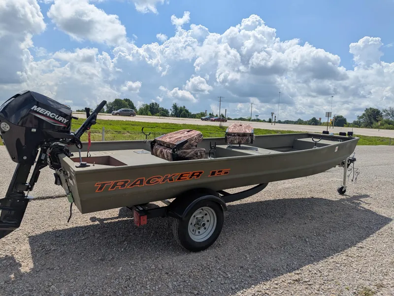 Slide: The Image of 2025 Tracker Grizzly 15 Jon boat with Mercury motor on trailer, under a cloudy sky. - 24