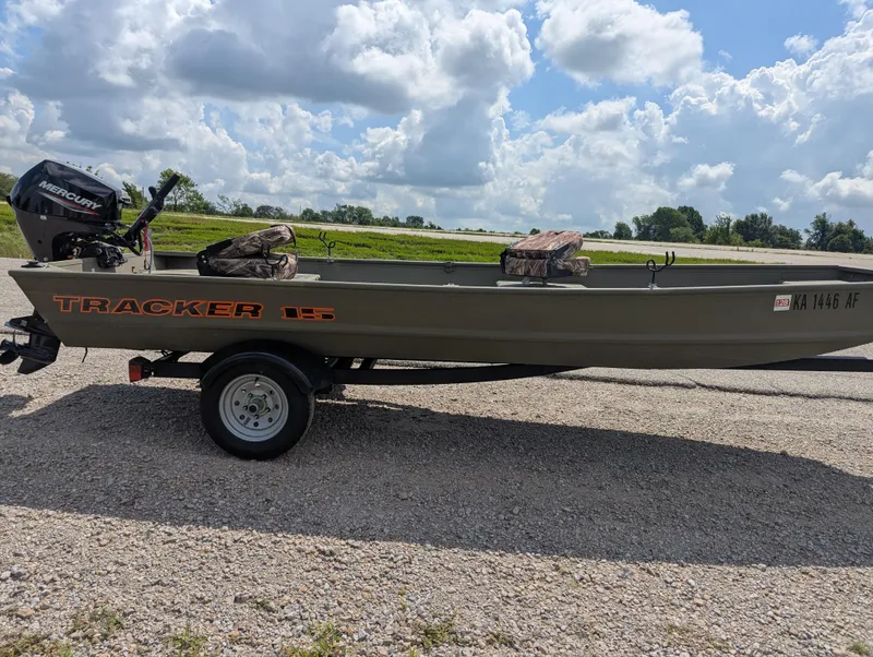 Slide: The Image of 2025 Tracker Grizzly 15 Jon boat on trailer, parked on gravel road under cloudy sky. - 25