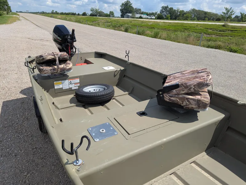 Slide: The Image of 2025 Tracker Grizzly 15 Jon boat with motor, camo seats, and spare tire on roadside. - 29