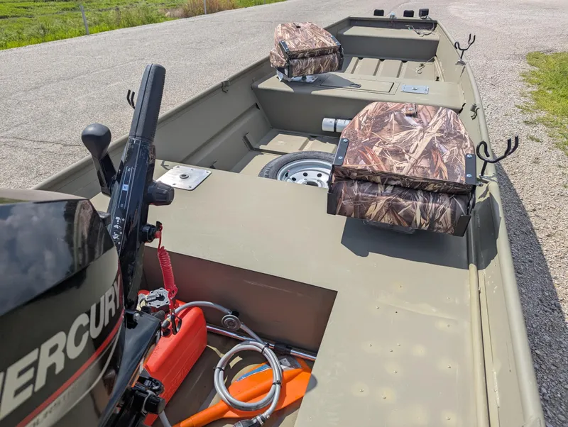 Slide: The Image of 2025 Tracker Grizzly 15 Jon boat with camo seats and Mercury motor on a gravel path. - 30