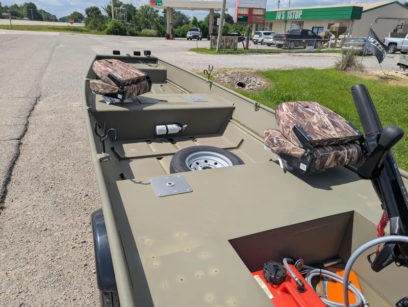 Slide: The Image of 2025 Tracker Grizzly 15 Jon boat with camo seats, parked near a gas station. - 31