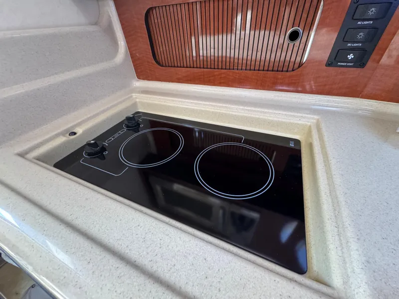 Slide: The Image of 2005 Sea Ray 320 Sundancer kitchen with sleek electric stovetop and wooden cabinetry. - 17