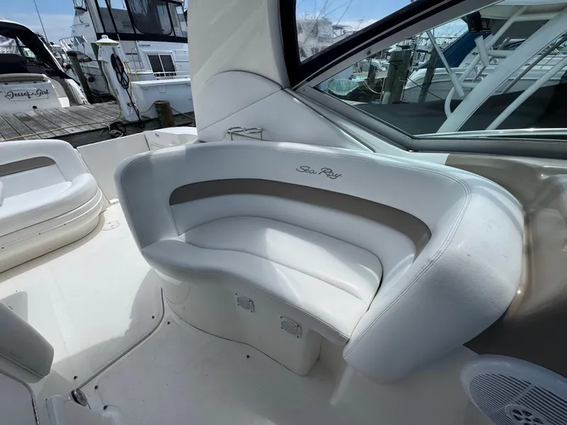 Slide: The Image of 2005 Sea Ray 320 Sundancer boat interior with white seating and docked boats in background. - 6