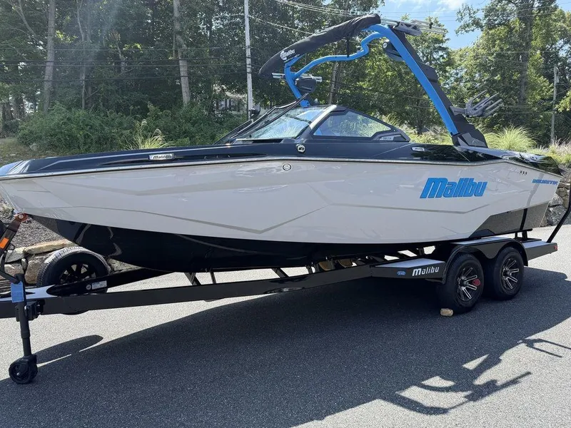 The Image of 2026 Malibu 22 LSV boat on trailer, parked outdoors, with sleek design and blue accents. - 1