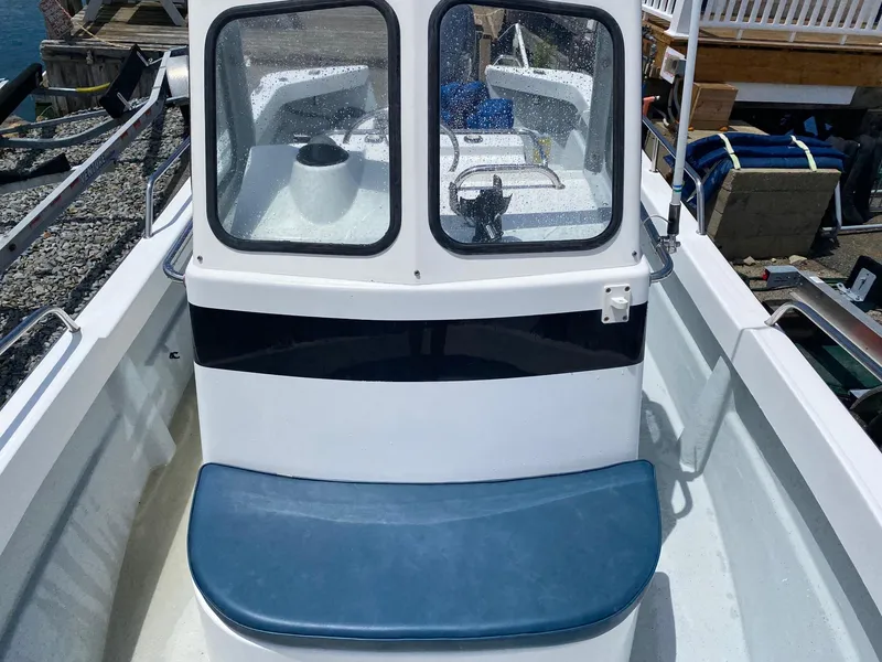 Slide: The Image of 1999 Maritime Skiff 20D boat with blue seating and enclosed cabin, docked on gravel. - 10