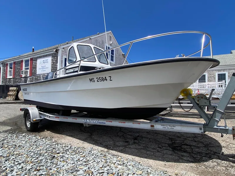 Slide: The Image of 1999 Maritime Skiff 20D on trailer, parked outside a marina under clear blue sky. - 2