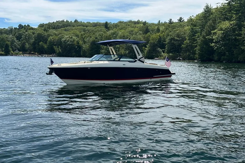 Slide: The Image of 2026 Chris-Craft Sportster 28 boat on a scenic lake with lush green trees. - 2