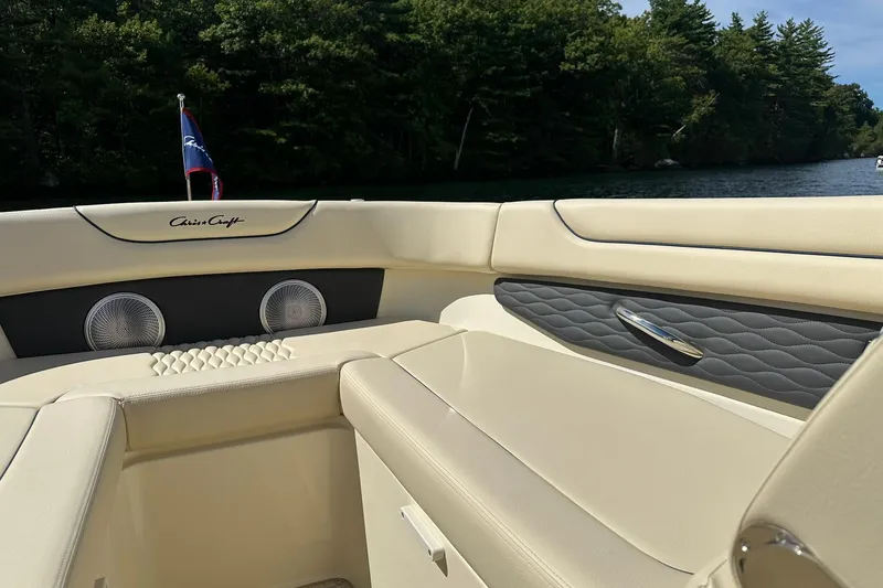 Slide: The Image of 2026 Chris-Craft Sportster 28 interior with beige seating, lake view, and lush greenery. - 21
