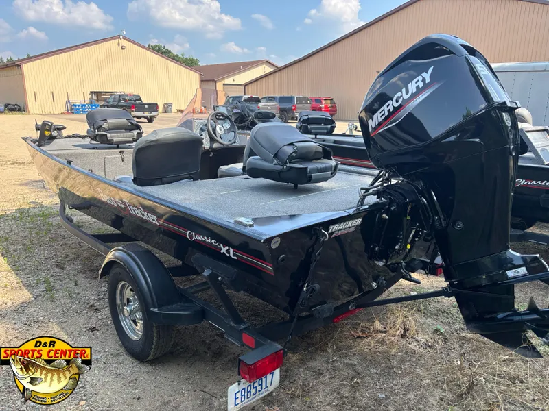 Slide: The Image of 2021 Tracker Bass Tracker Classic XL boat with Mercury engine, parked outdoors near buildings. - 2