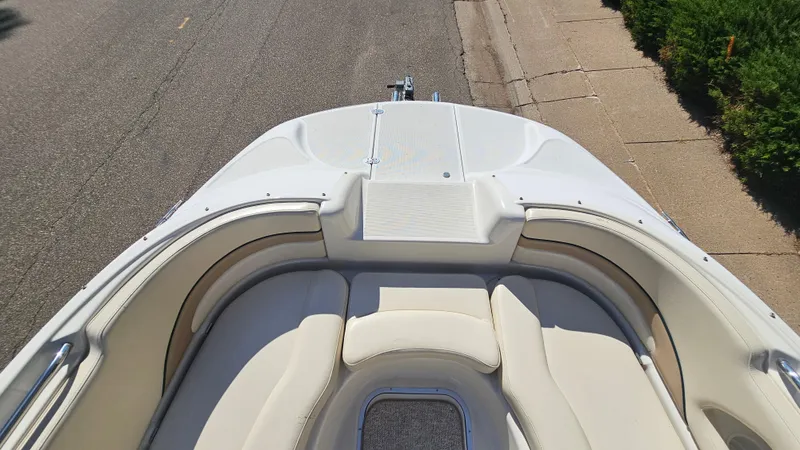 Slide: The Image of 2000 Chris-Craft 262 Sport Deck boat with white cushioned seating, parked on a street. - 16