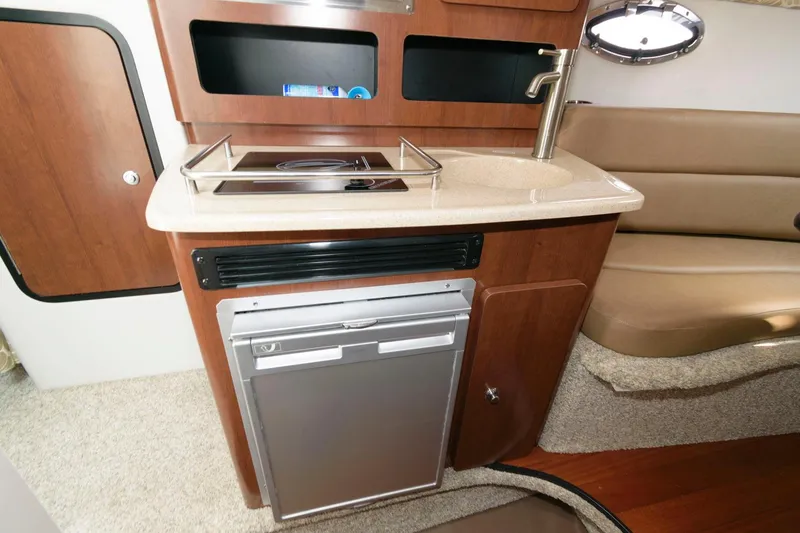 Slide: The Image of 2021 Crownline 264 CR boat interior with kitchenette, featuring sink, stove, and mini-fridge. - 13