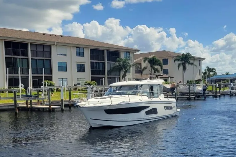 Slide: The Image of 2021 Jeanneau NC 1095 boat cruising near waterfront buildings under a blue sky. - 1